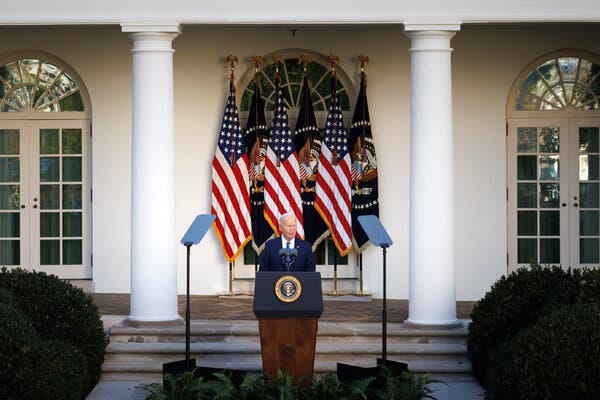 President Biden speaking from behind a lectern in front of several American flags outside the White House.