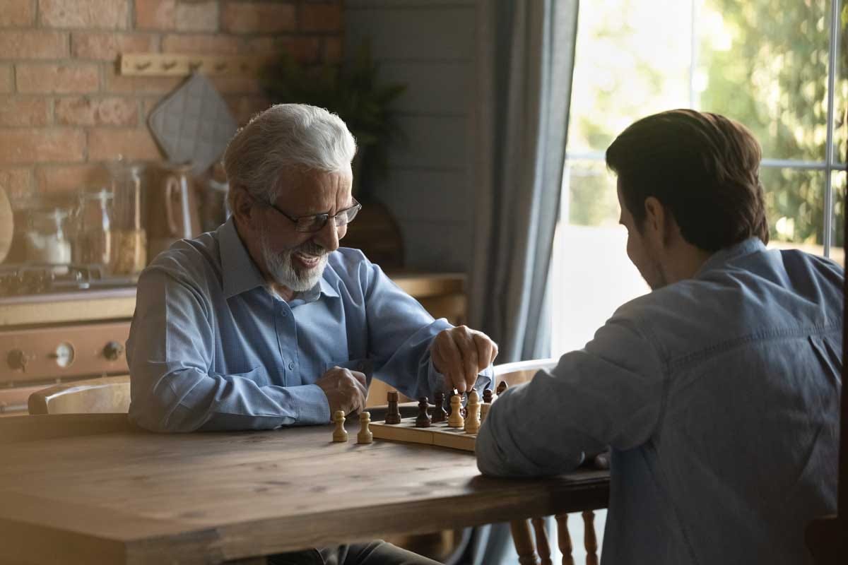 Battle at chessboard. Enthusiastic old father play friendly chess match at home with grownup son.