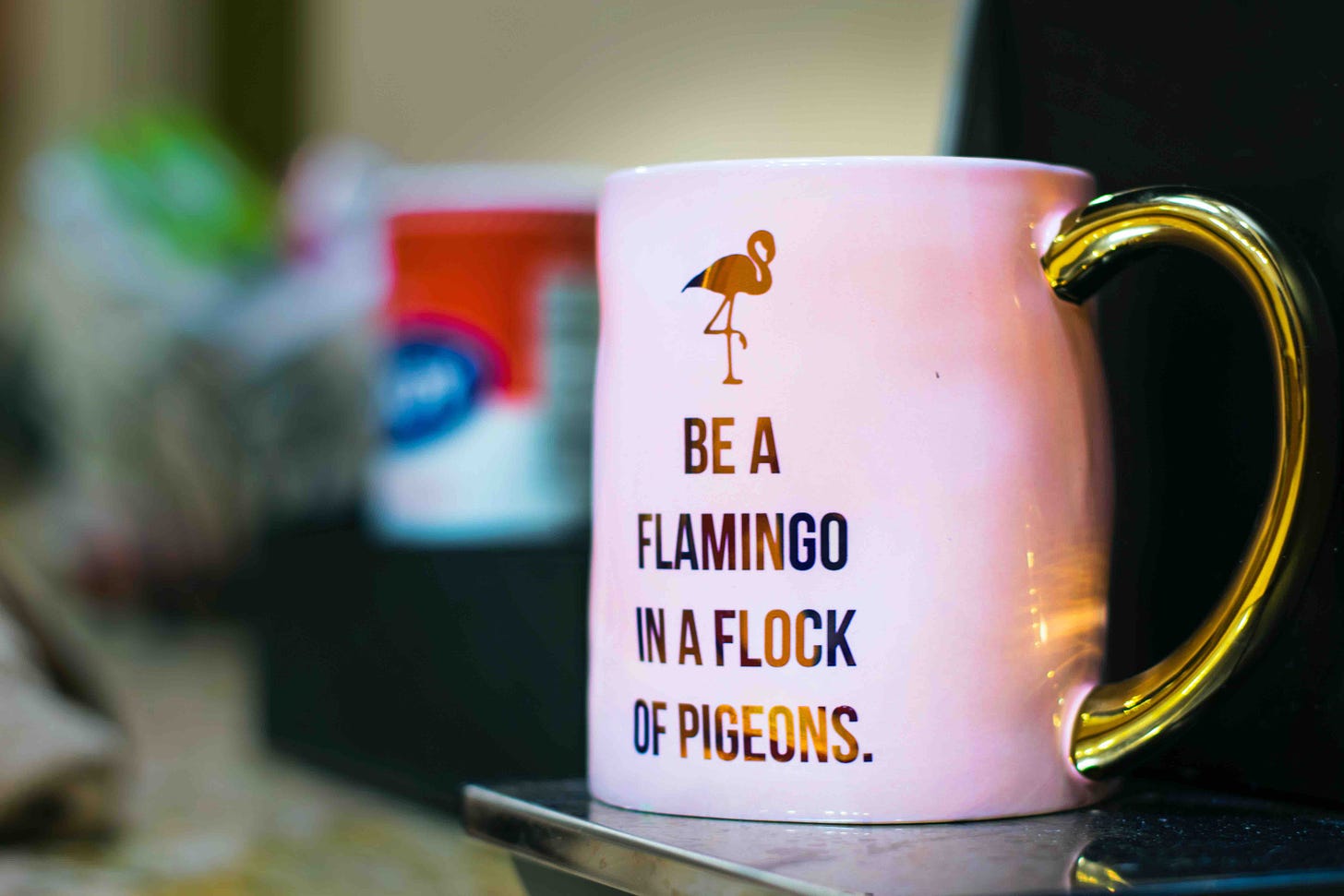 Pink mug with gold text saying Be a Flamingo in a Flock of Pigeons to illustrate how to doing the opposite often raises vibration