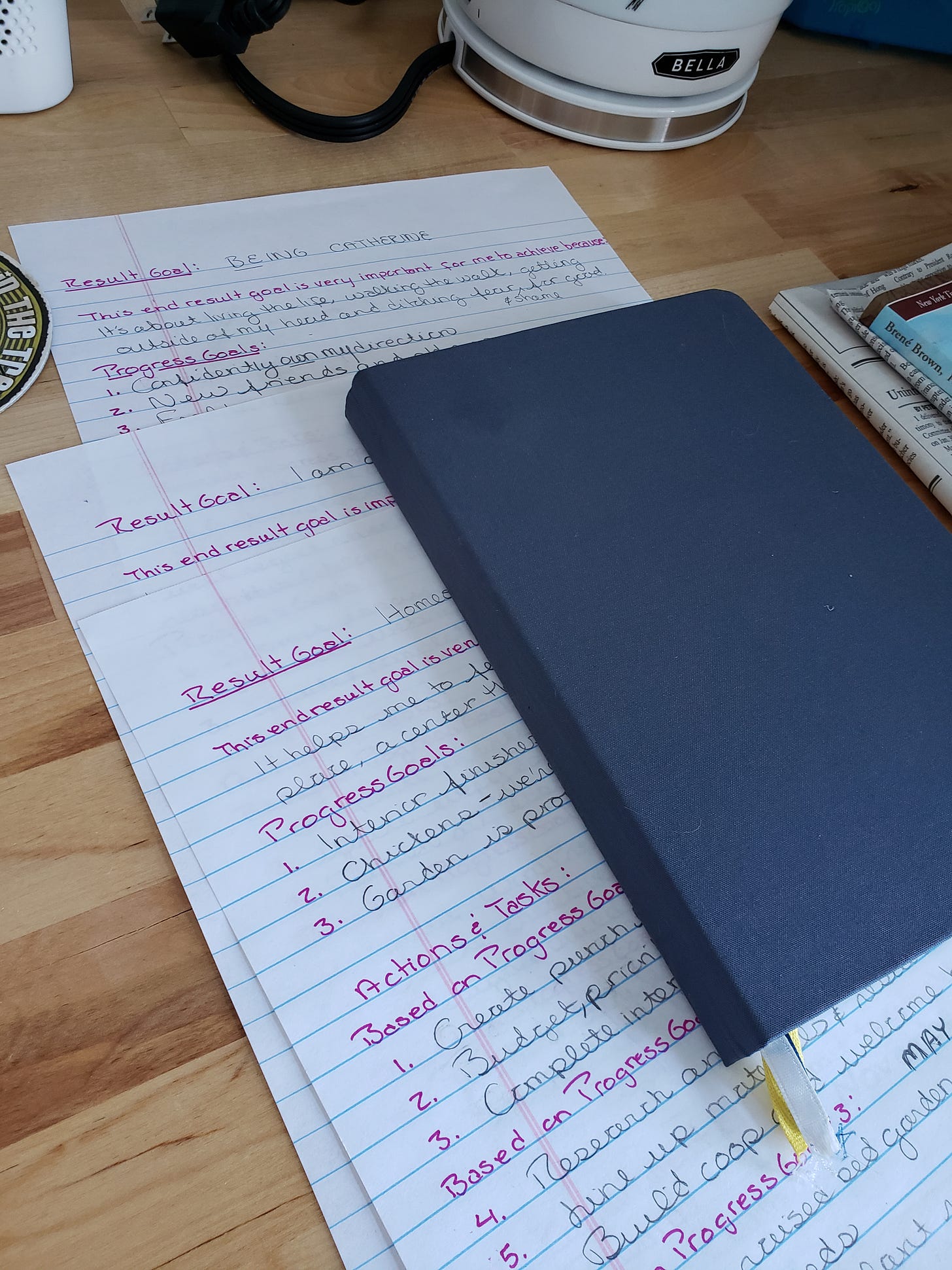 A blue notebook partially covers three pages of lined paper with lists of goals and progress