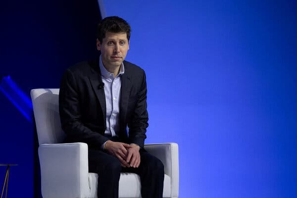 Sam Altman, wearing a dark suit and light blue shirt, sits in a white chair against a light blue background.