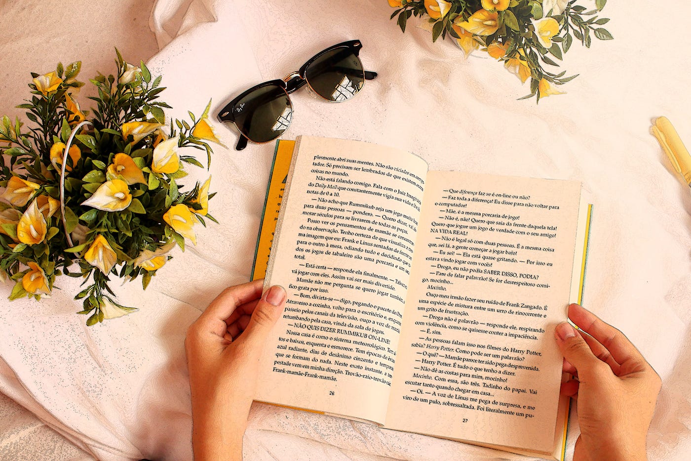 Open book on a table with yellow flowers and a pair of sunglasses.