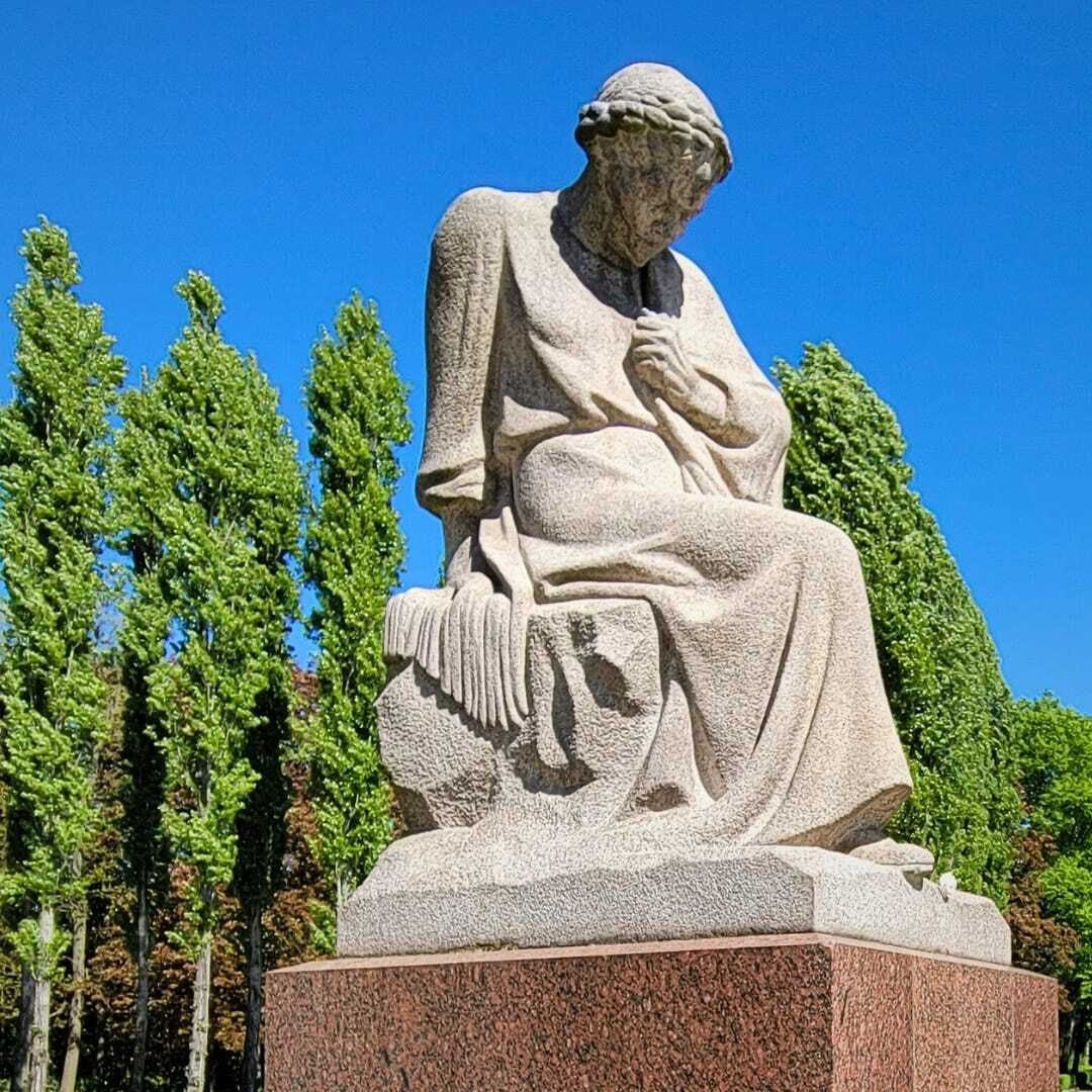 Statue of a woman sitting with her head bowed on top of a granite pillar.