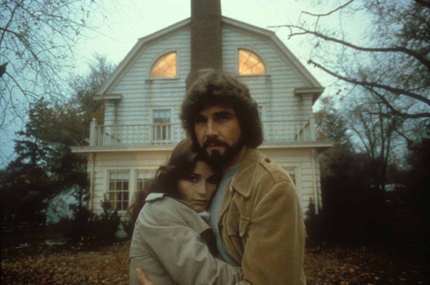 A promotional image from the first Amityville Horror film, with the two stars standing in front of the house