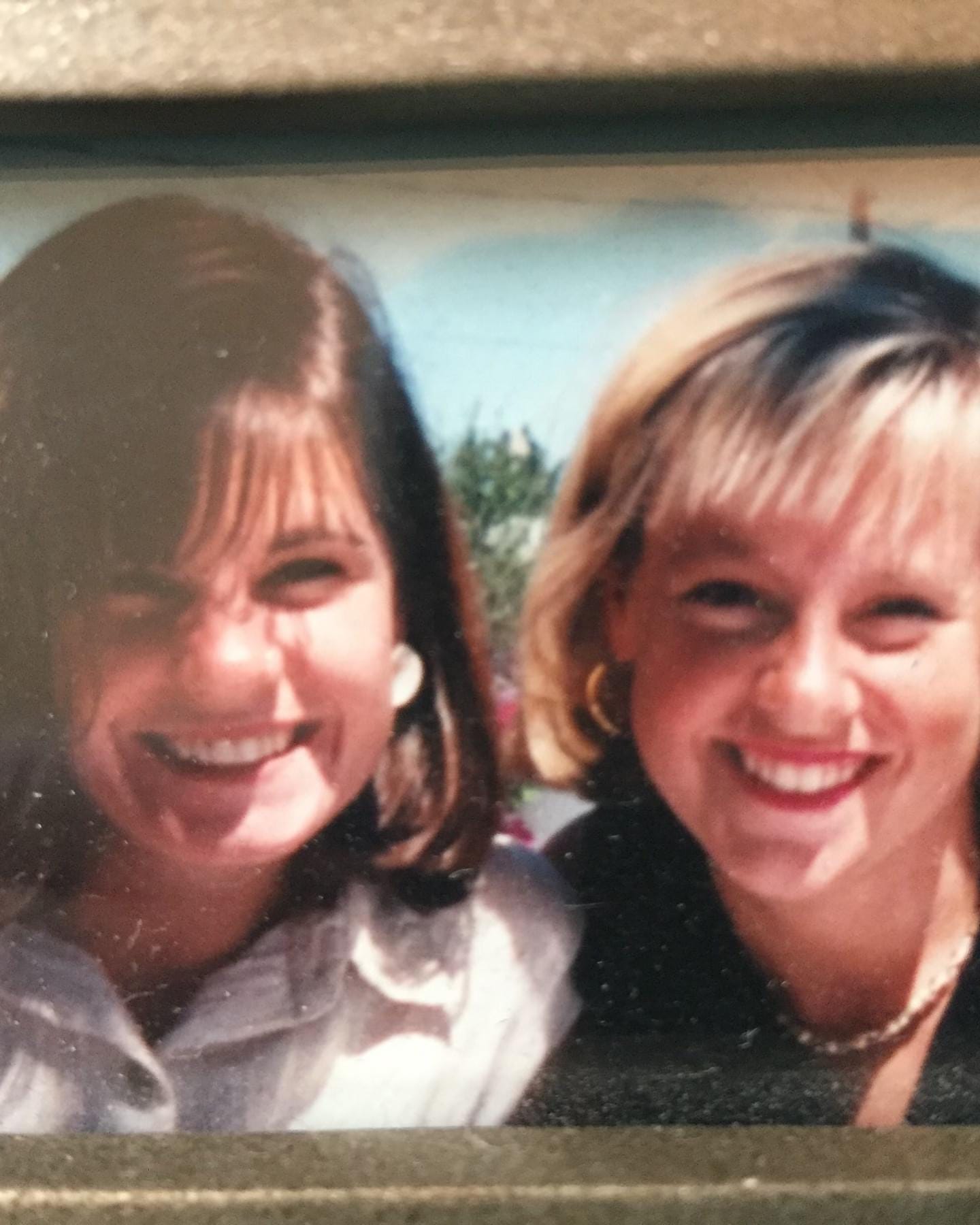 Two women smile for the camera. On the left is a brunette woman. On the right is a blonde woman. Both have hair that is above the shoulder. 