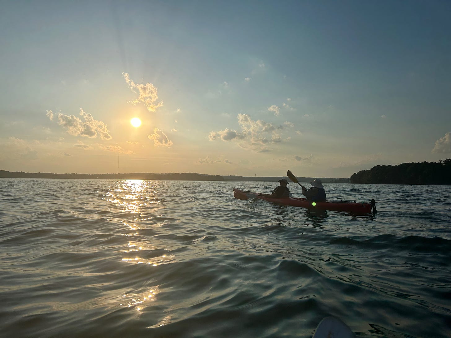 A photo of the ocean, a low sun and two people in a kayak