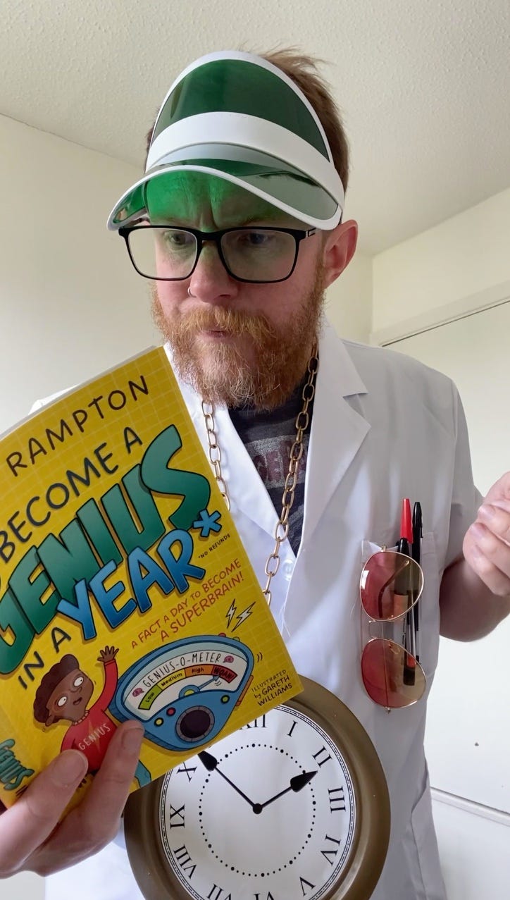 Me, in a lab coat, large clock medallion and green visor, with pens and aviator sunglasses in my pocket, reading from Become A Genius In A Year. Me, in a lab coat, large clock medallion and green visor, with pens and aviator sunglasses in my pocket, reading from Become A Genius In A Year.