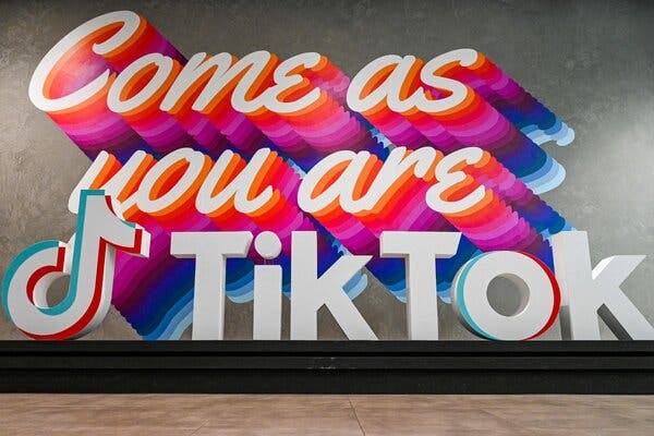 A logo sign for TikTok sits in front of a sign saying Come as you are.