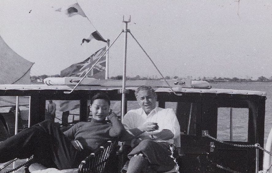 Anna May Wong sits next Chester Fritz on a sail boat with the wind blowing the flags in the background