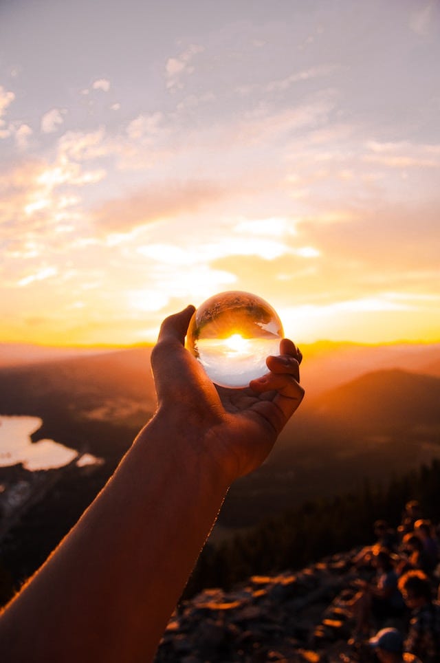 Photo of a person holding a crystal ball up to a sunset 