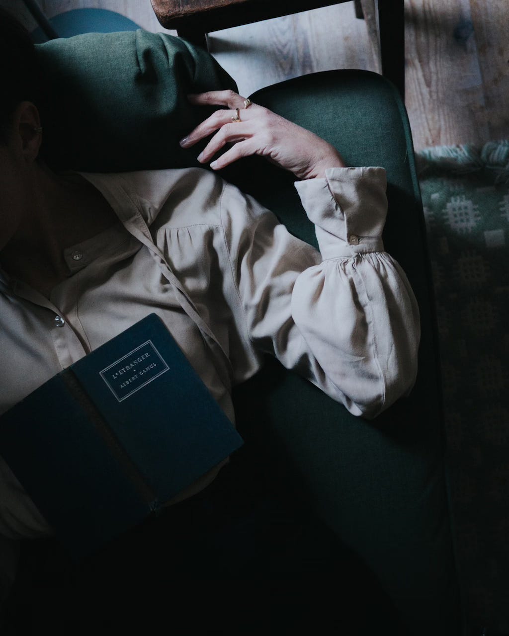 Overhead view of a woman lying on a green velvet sofa with a book on her chest