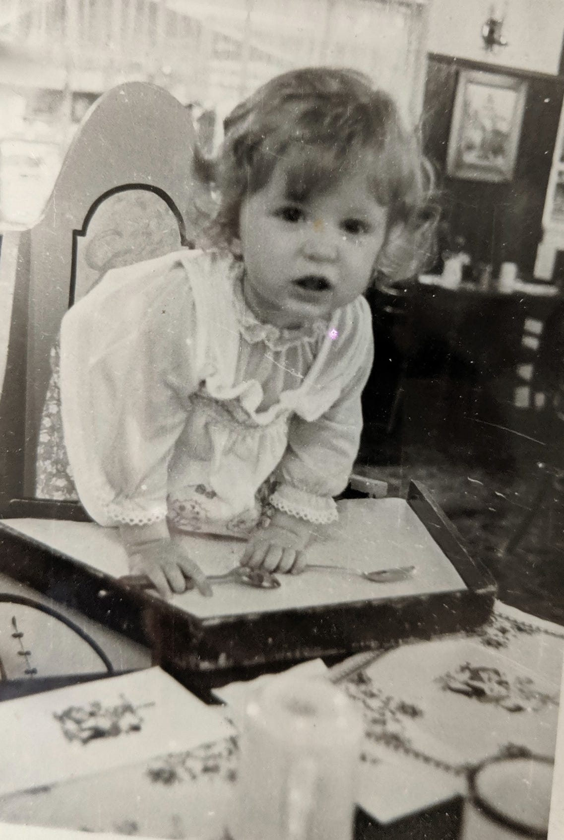 joanna schroeder as a child, black and white, curly haired child trying to escape a high chair and shouting