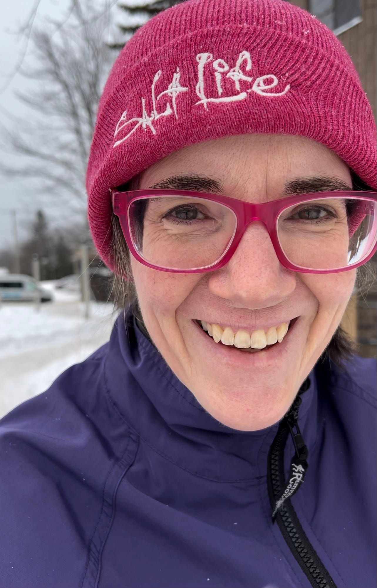 Woman in a pink toque, pink glasses smiling