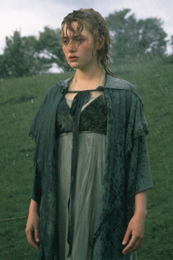 This may contain: a woman standing in the rain wearing a green cape and dress with an open collar