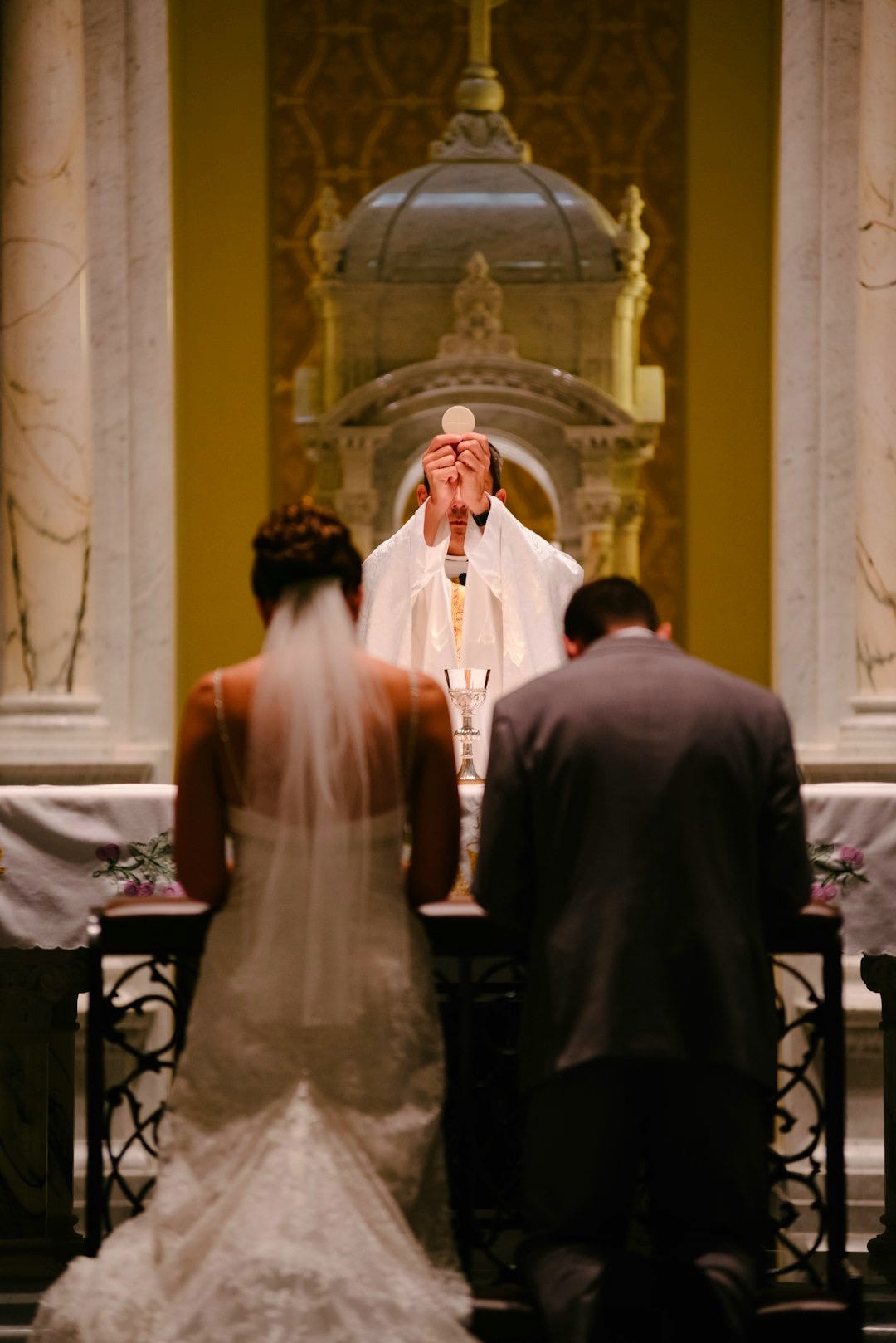 groom and bride kneeling in front of priest raising The Holy Sacrament groom and bride kneeling in front of priest raising The Holy Sacrament