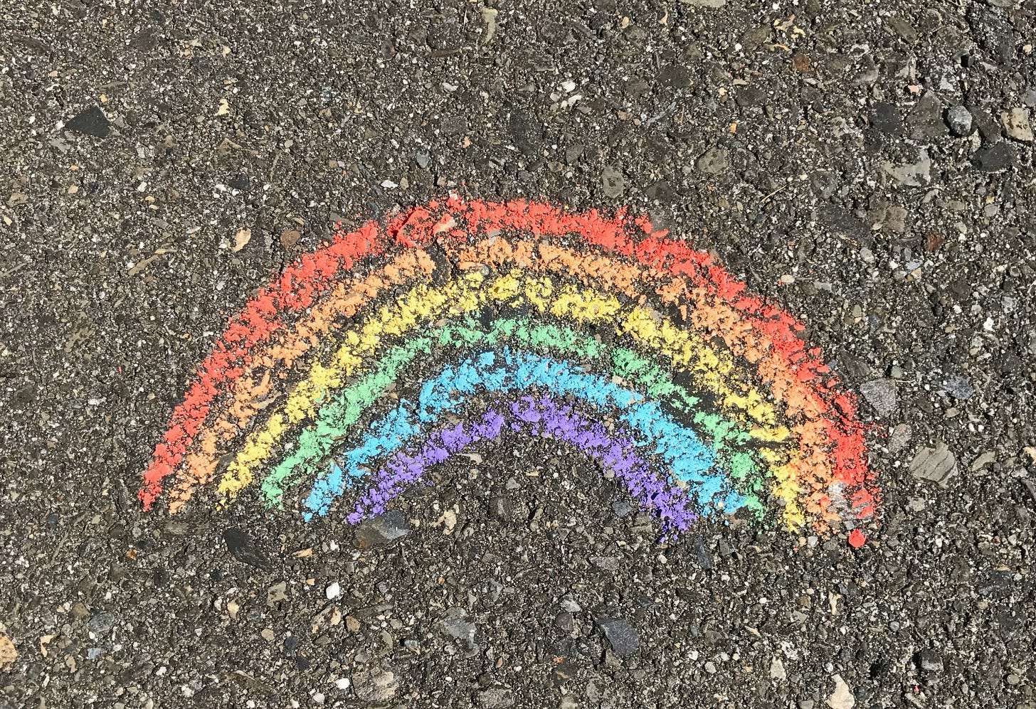 A simple rainbow with all the natural rainbow colors except for indigo (from red at the top to violet at the bottom) scrawled in sidewalk chalk on asphalt, with nothing else around it.