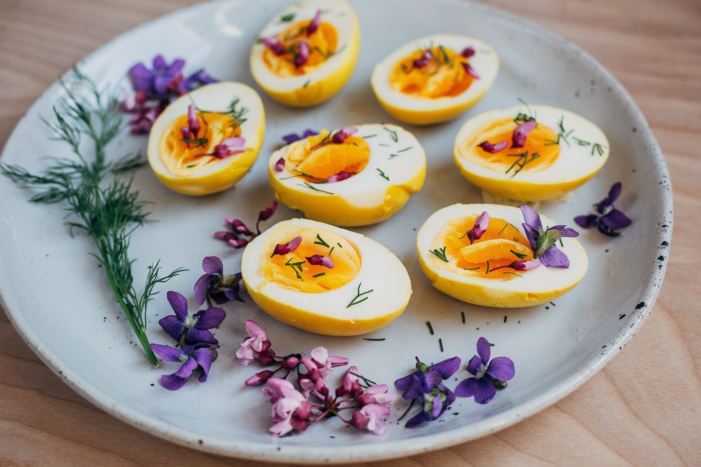 A plate of golden beet pickled eggs topped with herbs and red buds. 