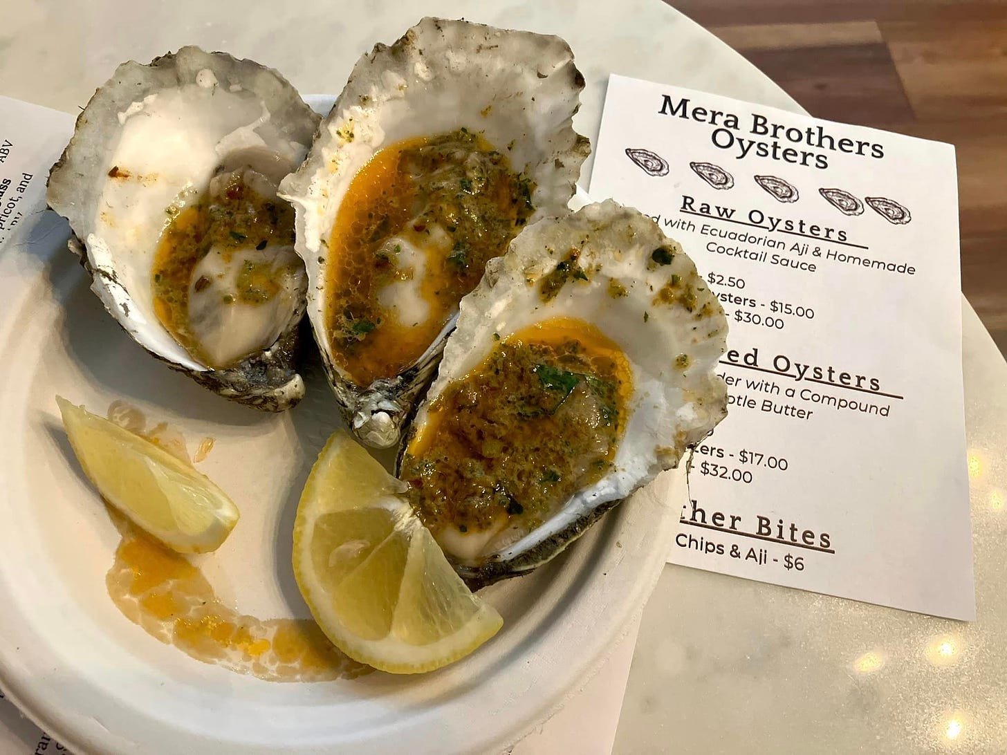 May be an image of text that says 'AY 19 ខ and ۱۹٩ Mera Oysters Brothers with Raw ( Ecuadoriar Cocktail Oysters sters Aji Sauce Homemade $2.50 sters- $30.00 $15.00 ed der with Oysters ptle Butter Compound ers $32.00 $17.00 her Bites Chips Aji $6'