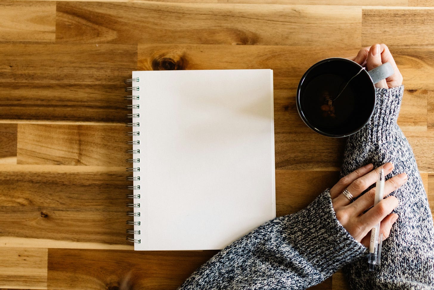 notebook on desk with person's hands holding a pen and coffee