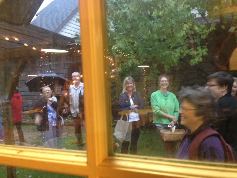 Viewed through two windowpanes framed by yellow muntins, a half-dozen people with baskets and bags smile in anticipation.