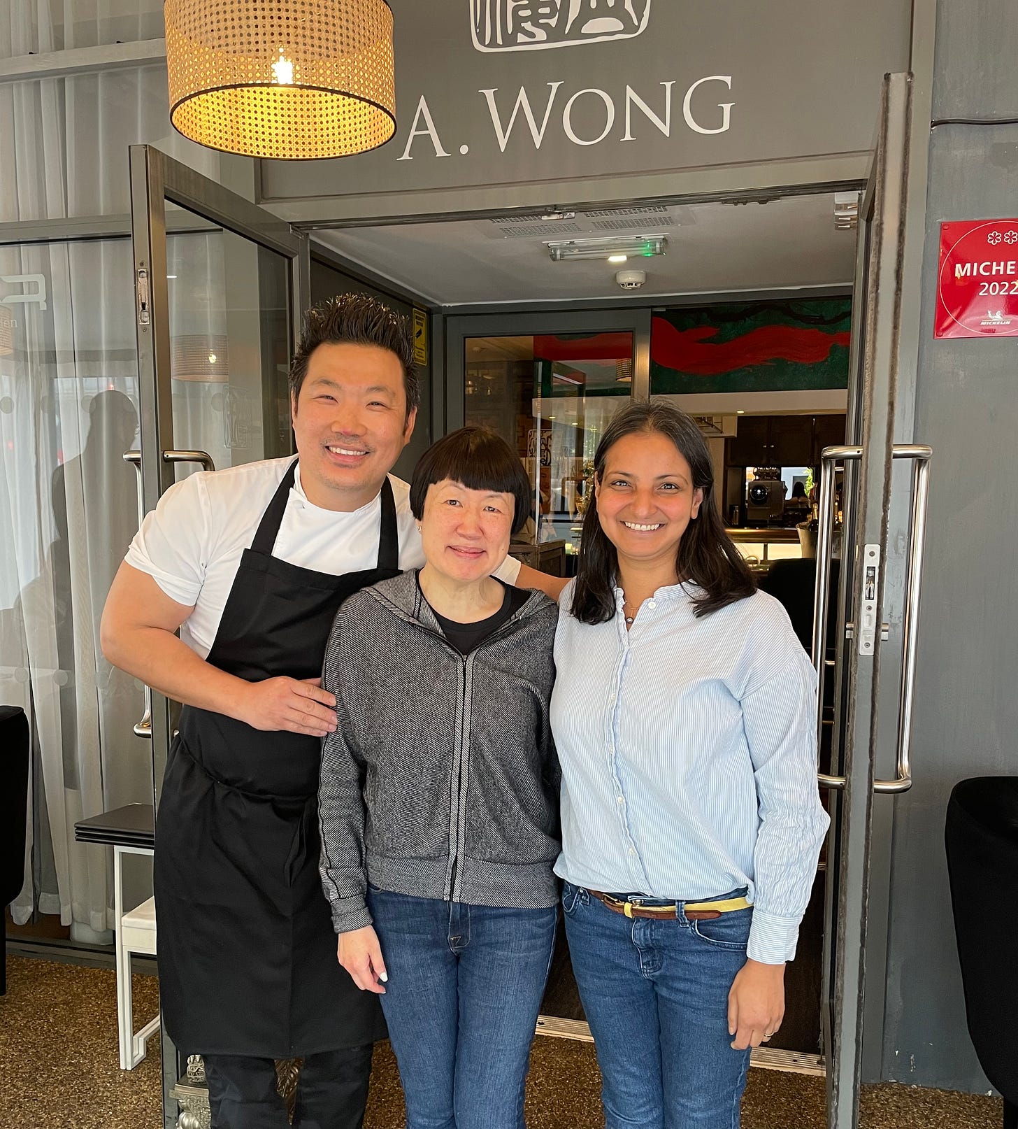 Three people outside the double doors of a restaurant smiling at the camera