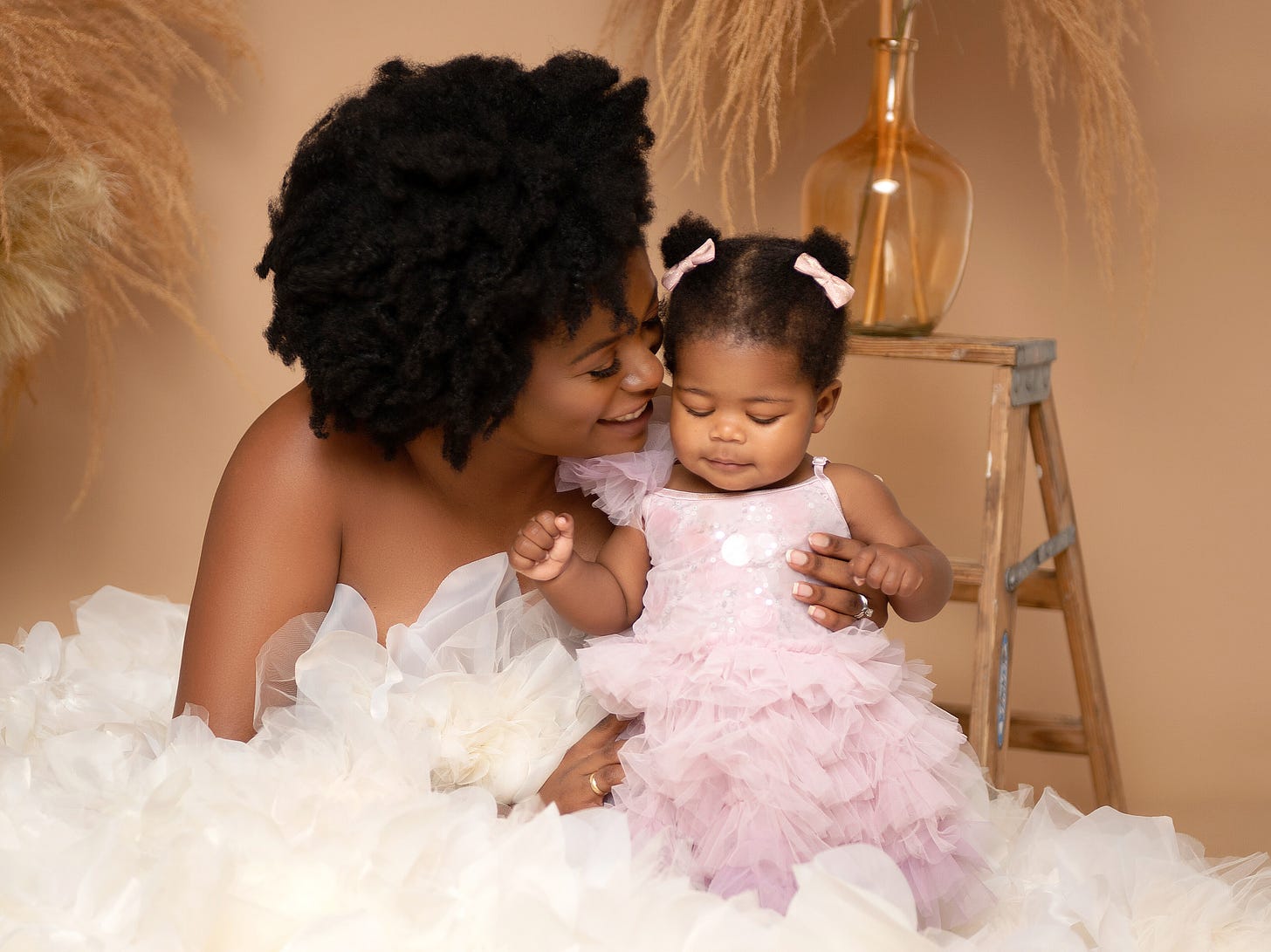 Picture of a Black mom wearing a white gown holding her toddler daughter wearing a purple gown
