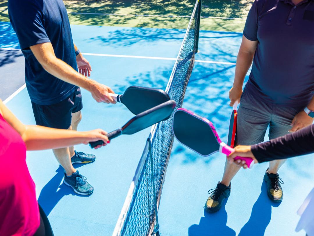 A photo from above, showing four pickleball players near the net, clicking their paddles together at the end of a game.