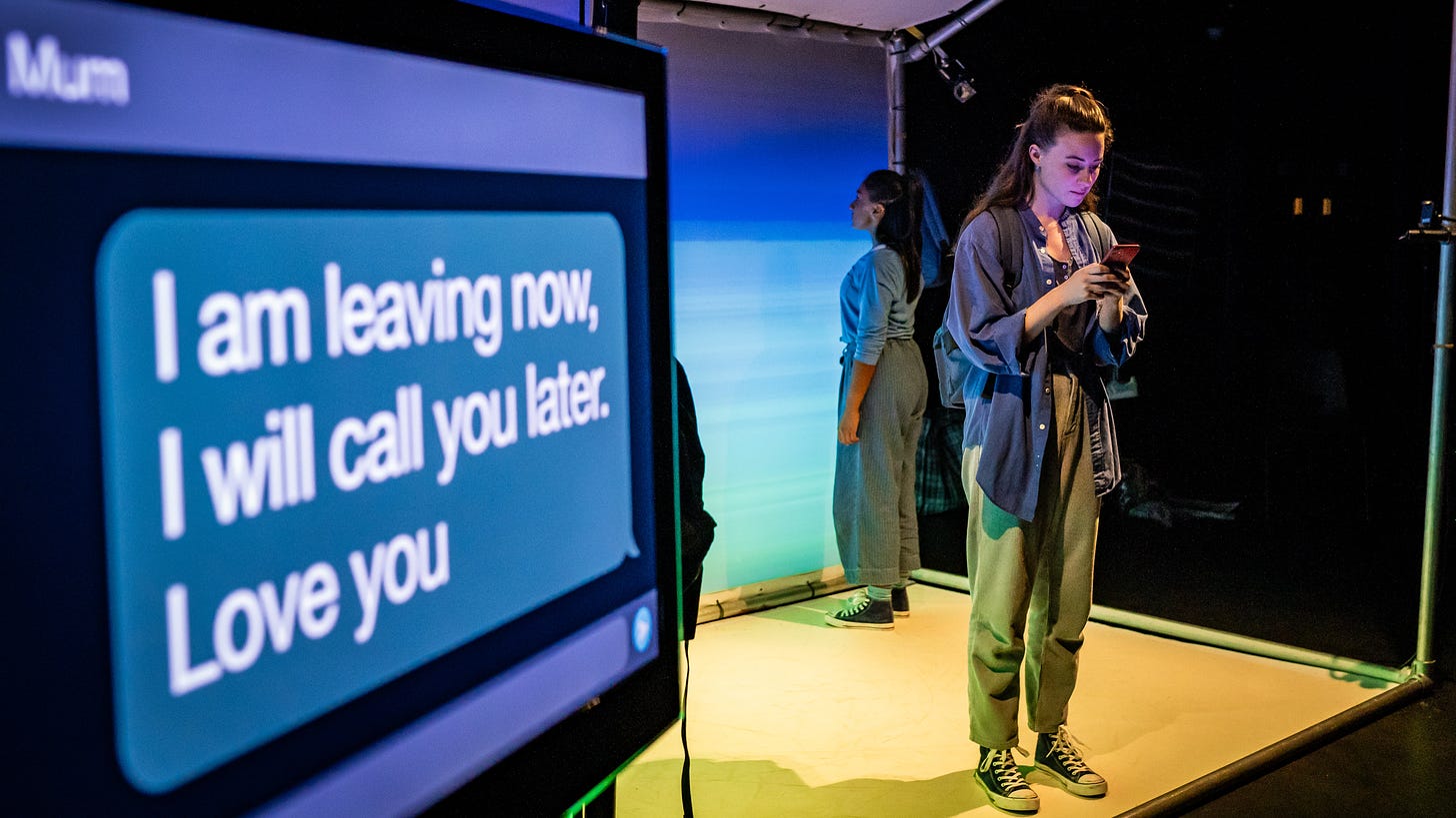 A young woman wearing loose clothes and trainers texts her mother. The phone screen is projected to one side and reads "I am leaving now, I will call you later. Love you.