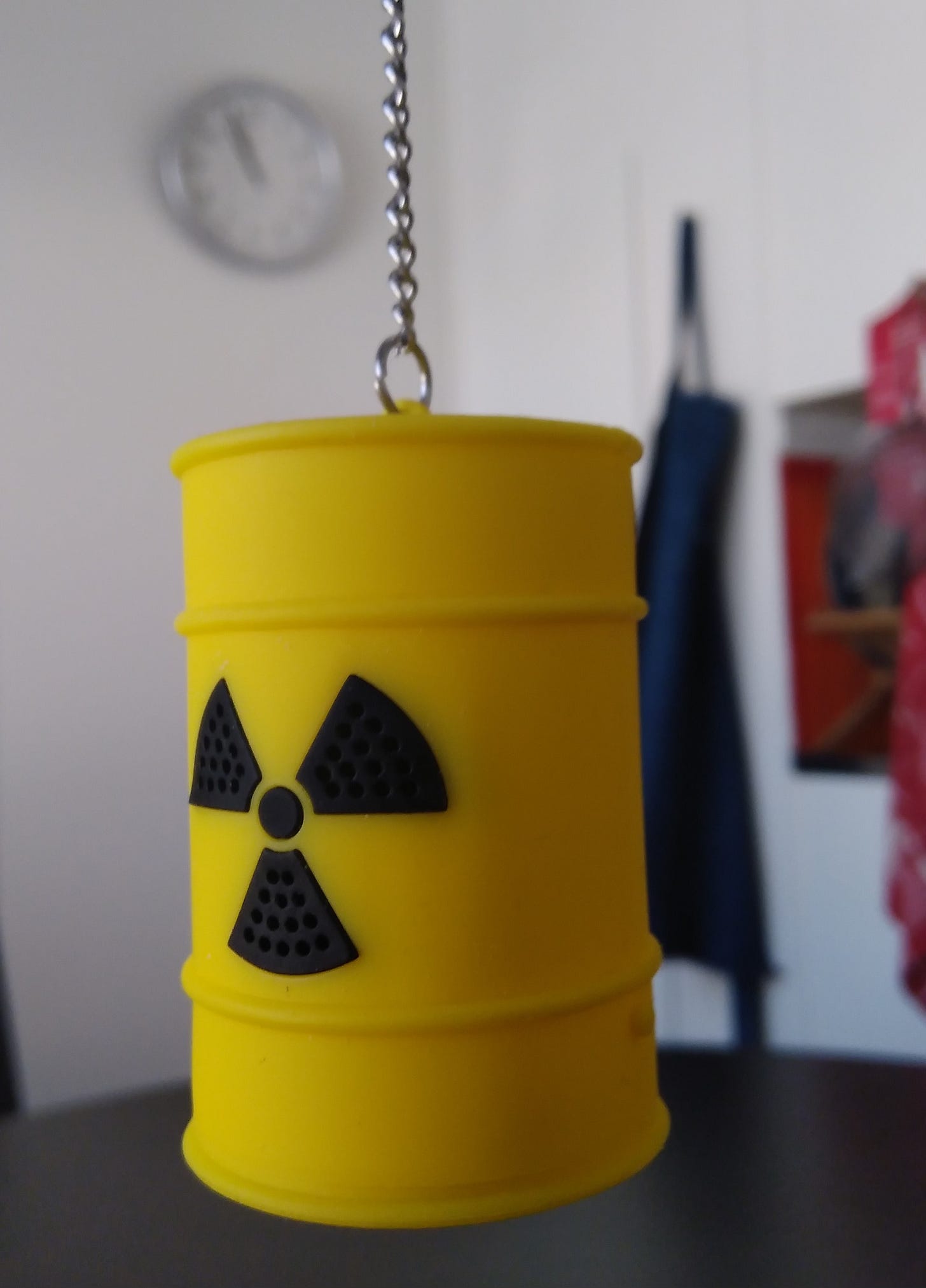 Bright yellow nuclear waste barrel hanging from a chain against a white kitchen wall