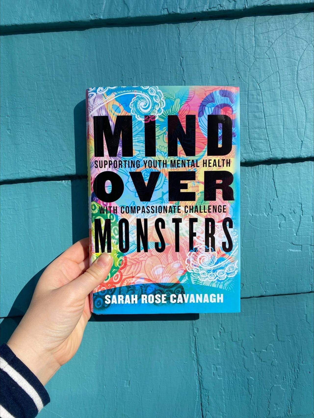 Copy of Mind Over Monsters held in front of a teal house