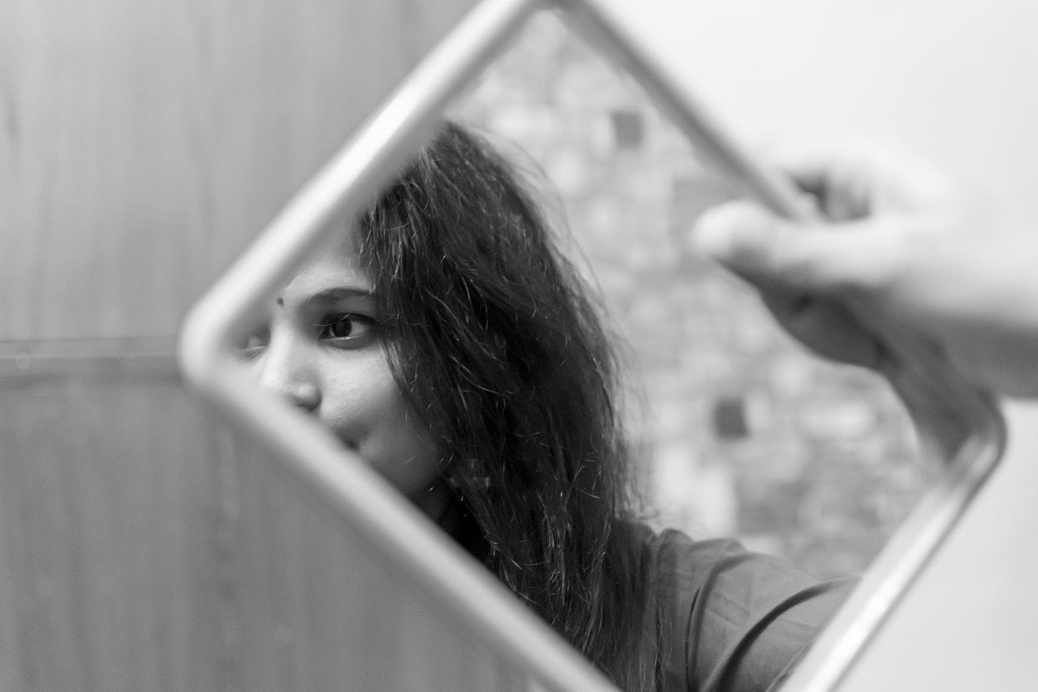 A young girl holds a mirror but is distracted and looks beyond.