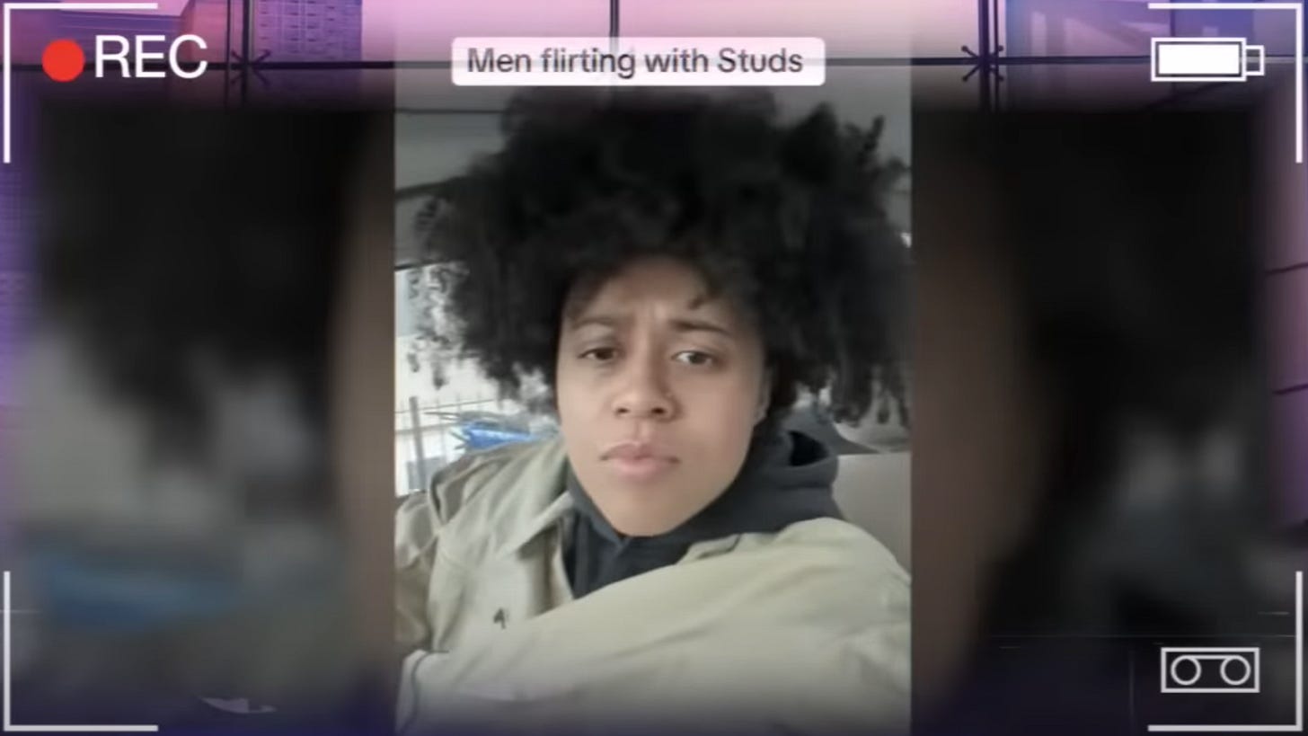 Biracial masculine-presenting lesbian stares into camera while sitting in the drivers seat of her car. Her hair is in a big puffy afro and she is wearing a biege jacket. Her caption reads, “Men Flirting With Studs”