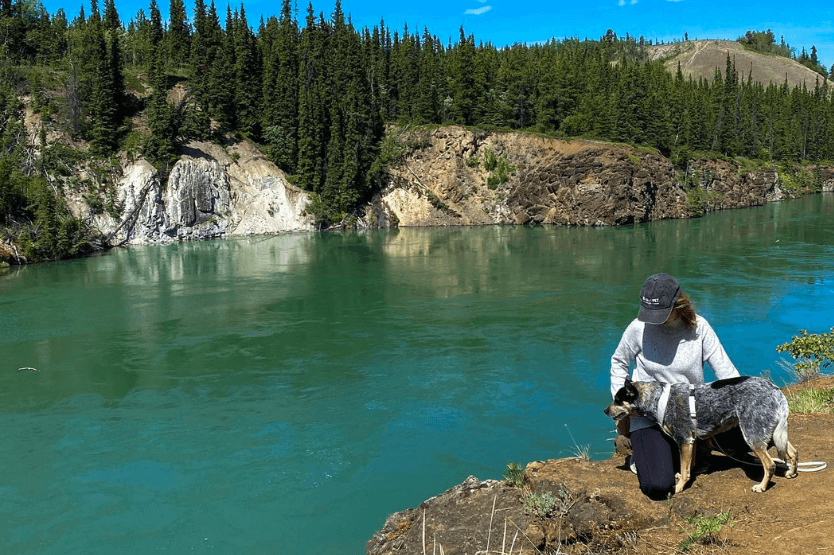 Haley, a young woman, and Scout, an Australian cattle dog, pose on the edge of Miles Canyon in the Yukon