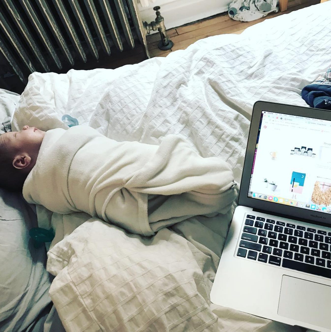 laptop open on bed next to sleeping baby