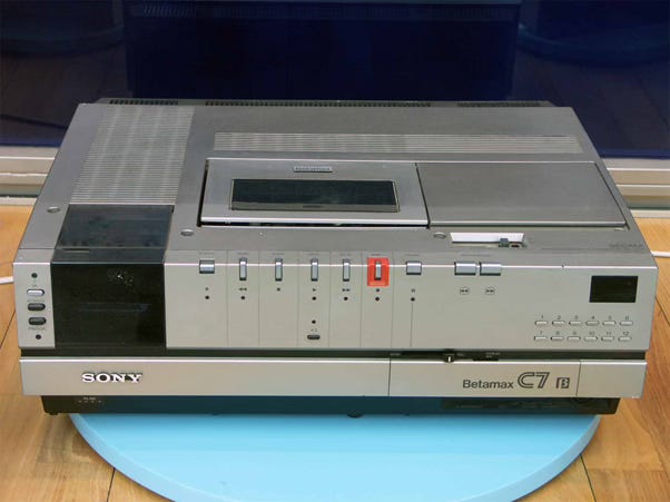 The image shows a Sony Betamax C7 B video player/recorder. It is a retro-style audio/video equipment with a sleek silver and black design. The device has various controls and buttons on the front panel, including a display screen. The Betamax C7 B was a popular home video format produced by Sony in the 1980s as a competitor to the VHS format.