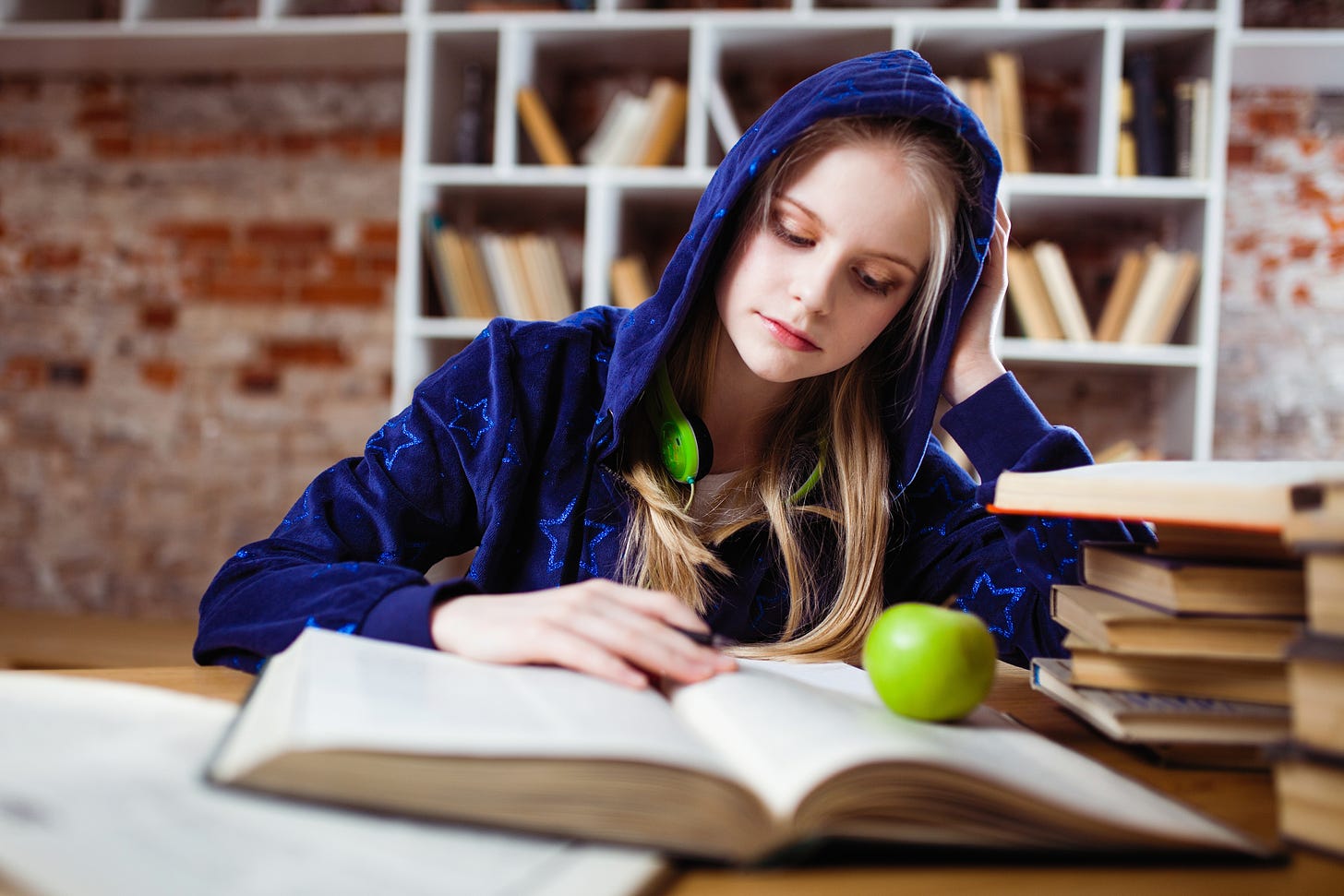 Blonde haird girl wearing a blue hoodie studying.