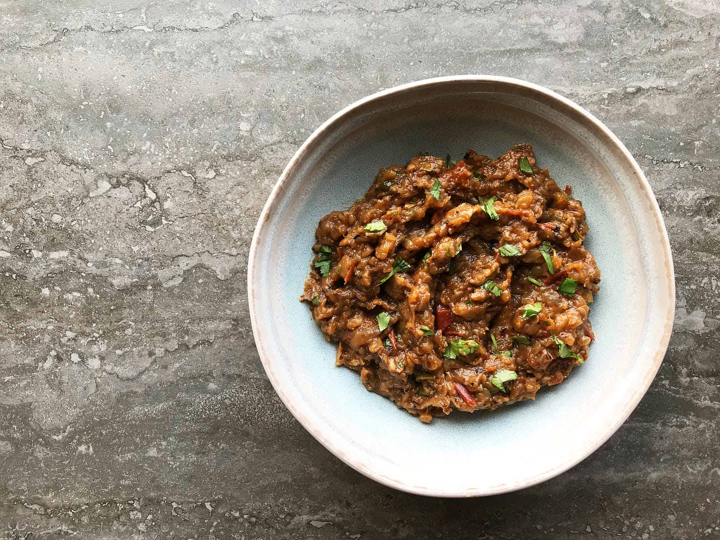 A bowl so aubergine masala: Golden waves of soft aubergine mixed with red tomato and flecked with green coriander leaf.