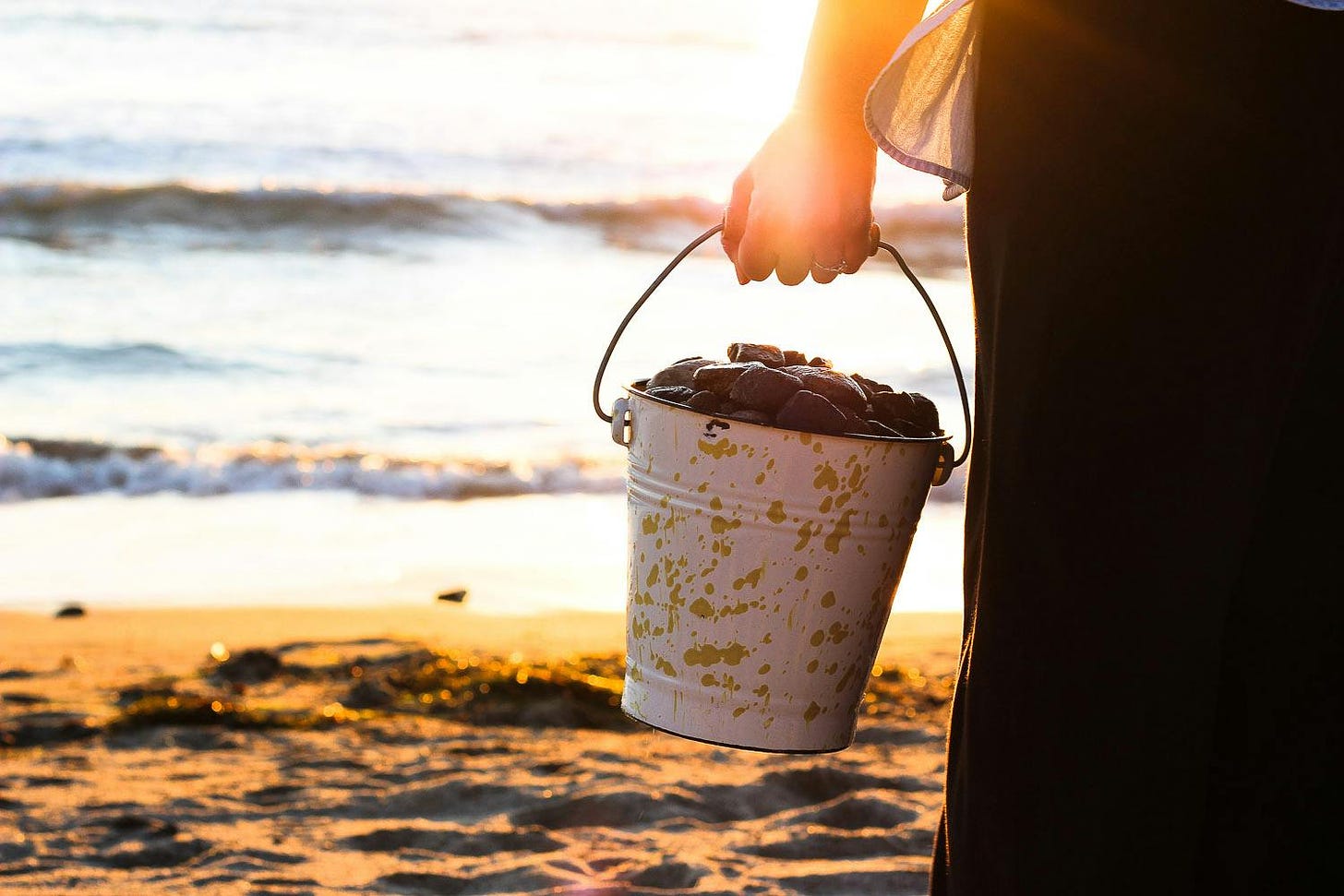Woman holding a bucket of rocks near the ocean