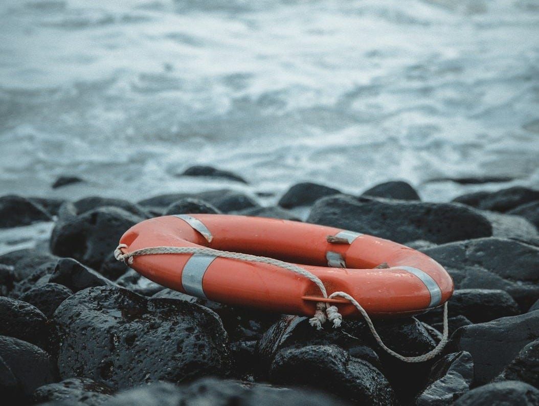 red inflatable ring on black rock near body of water during daytime red inflatable ring on black rock near body of water during daytime