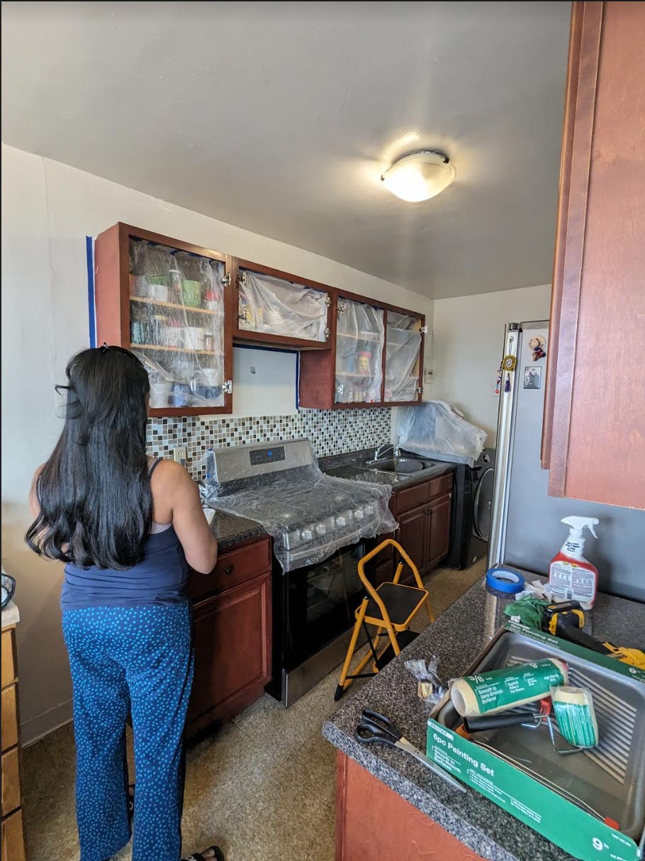 The brown cabinets from this kitchen are removed to show plastic covering the kitchen items