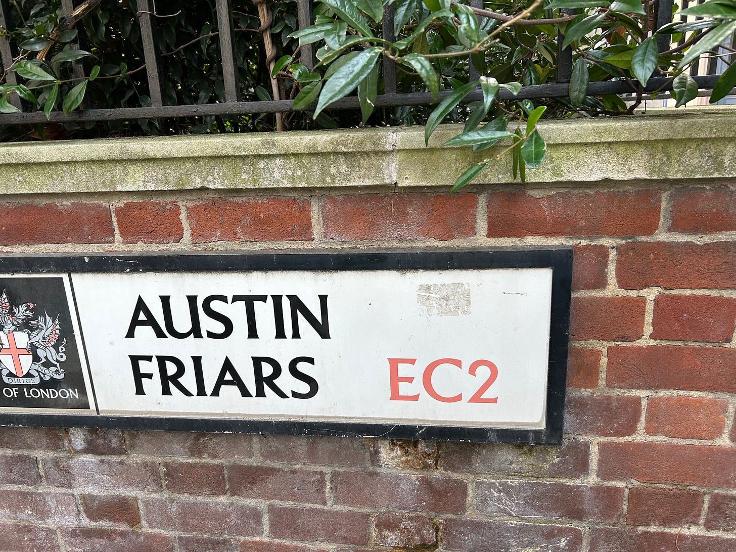 A City of London road sign for Austin Friars, attached to a brick wall.