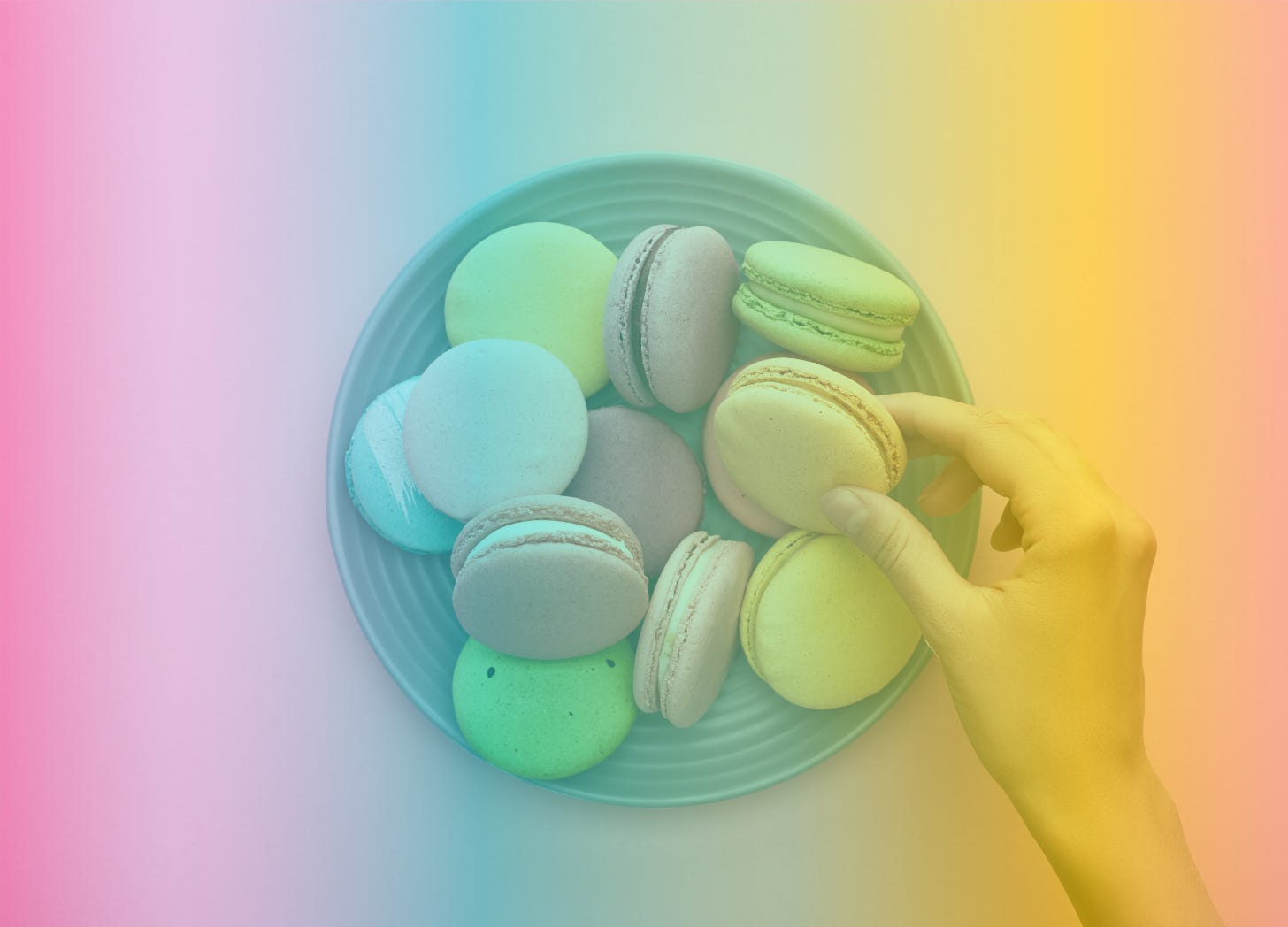 A rainbow-filtered image of a hand reaching for a macaron on a plate of brightly-colored macarons