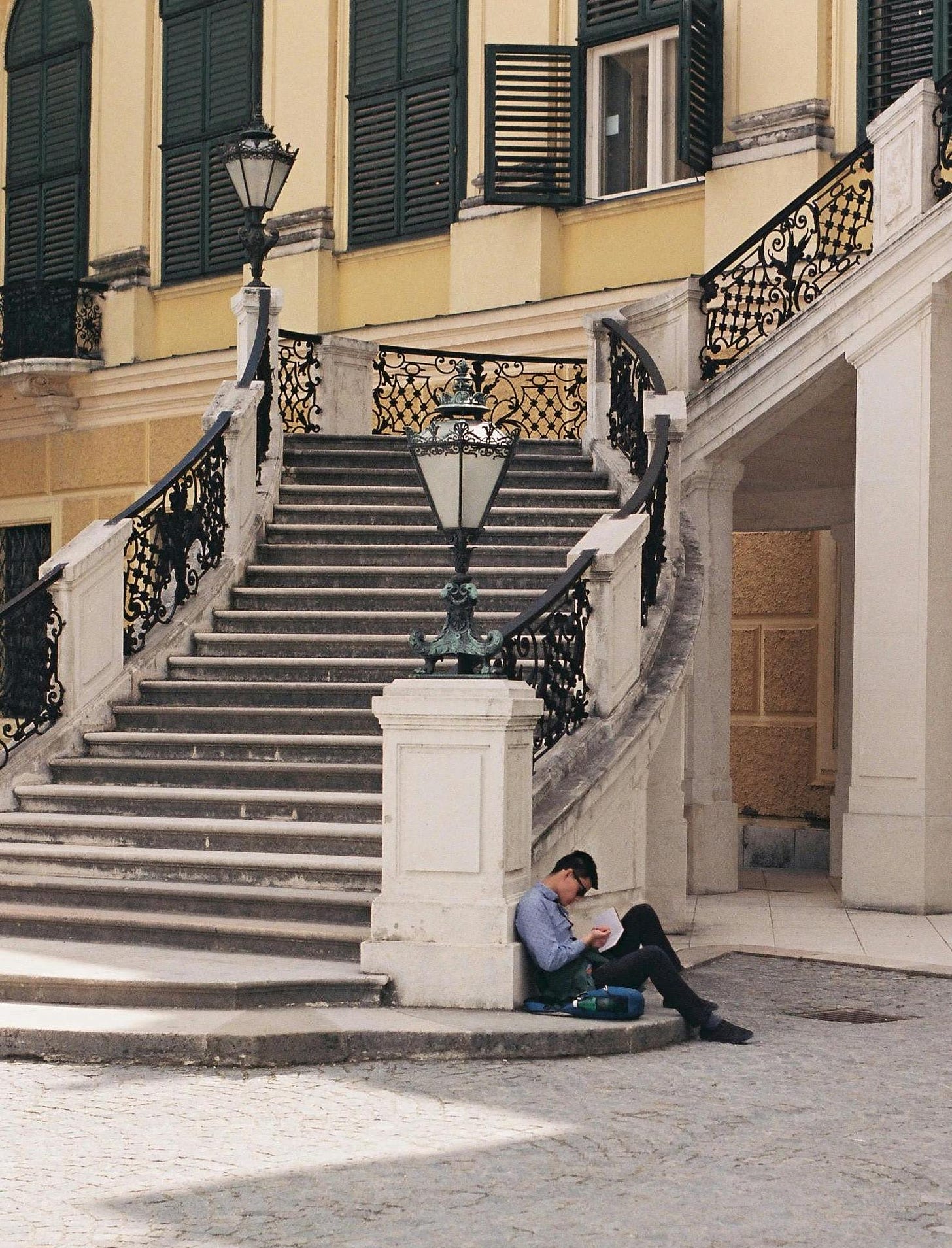 Young man sitting at the bottom of an ornate outdoor staircase reading a book