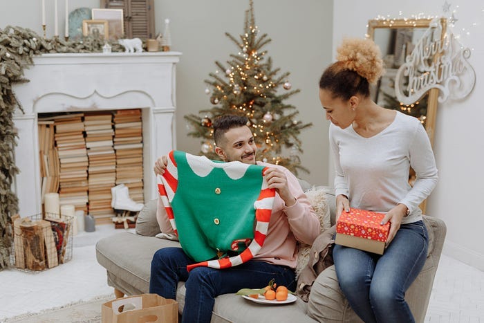 A man holding up an ugly sweater with a neutral look on his face. He doesn’t look too pleased about the prospect of wearing it.