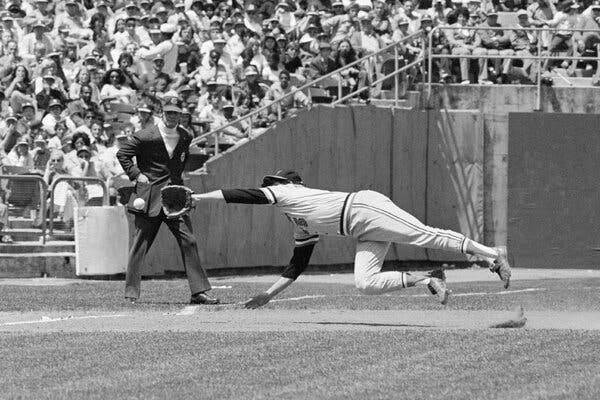 A black-and-white photo of Baltimore player Brooks Robinson in a horizontal midair position about to catch a baseball in flight that’s just in front of his glove.