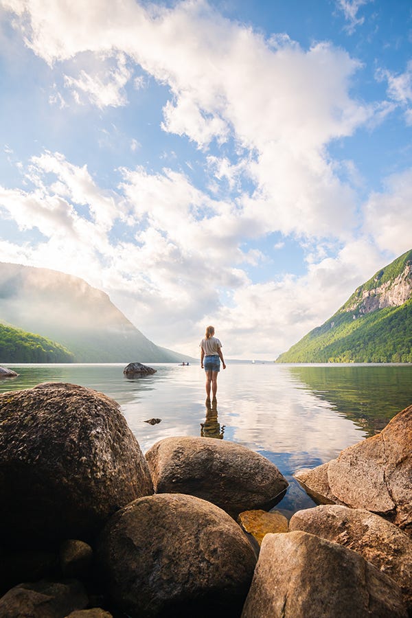 A person looks at the lake with mountains on either side of the view in the background.