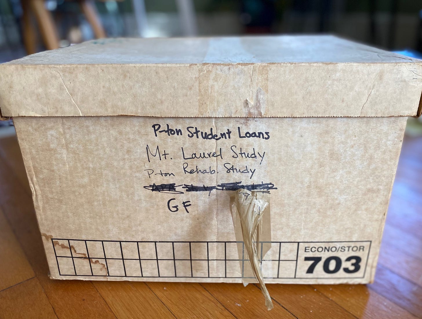 Discolored white bankers box with tape hanging off it. Box is labeled with P-ton Student Loans, Mt. Laurel study, P-ton Rehab Study, GF.