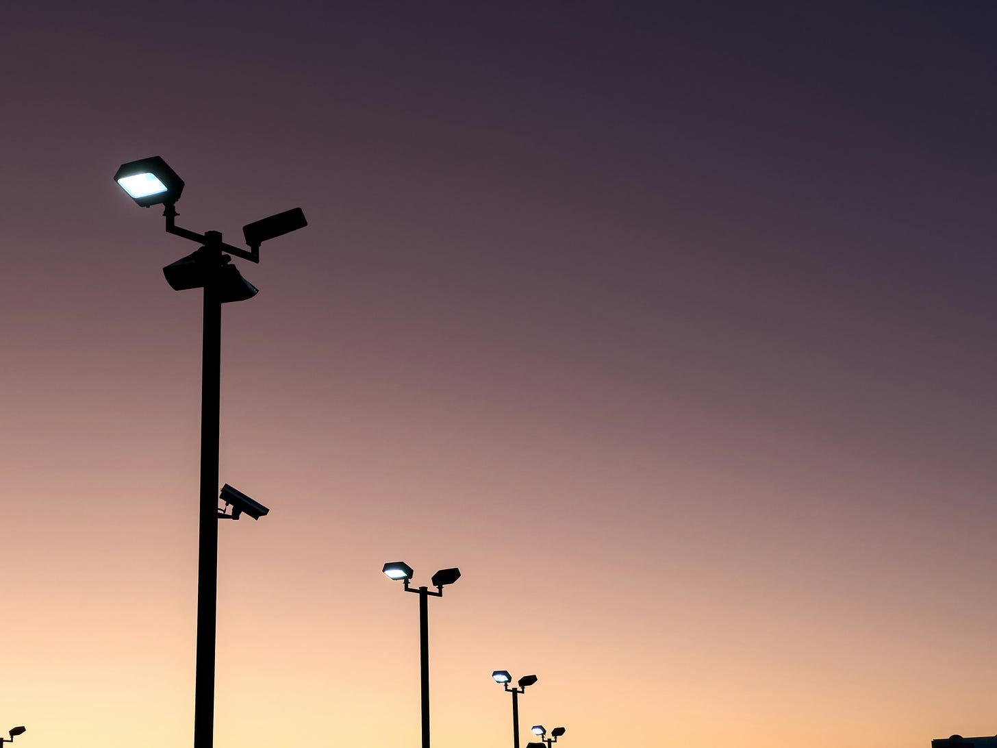 A photo of streetlights, one with a surveillance camera.