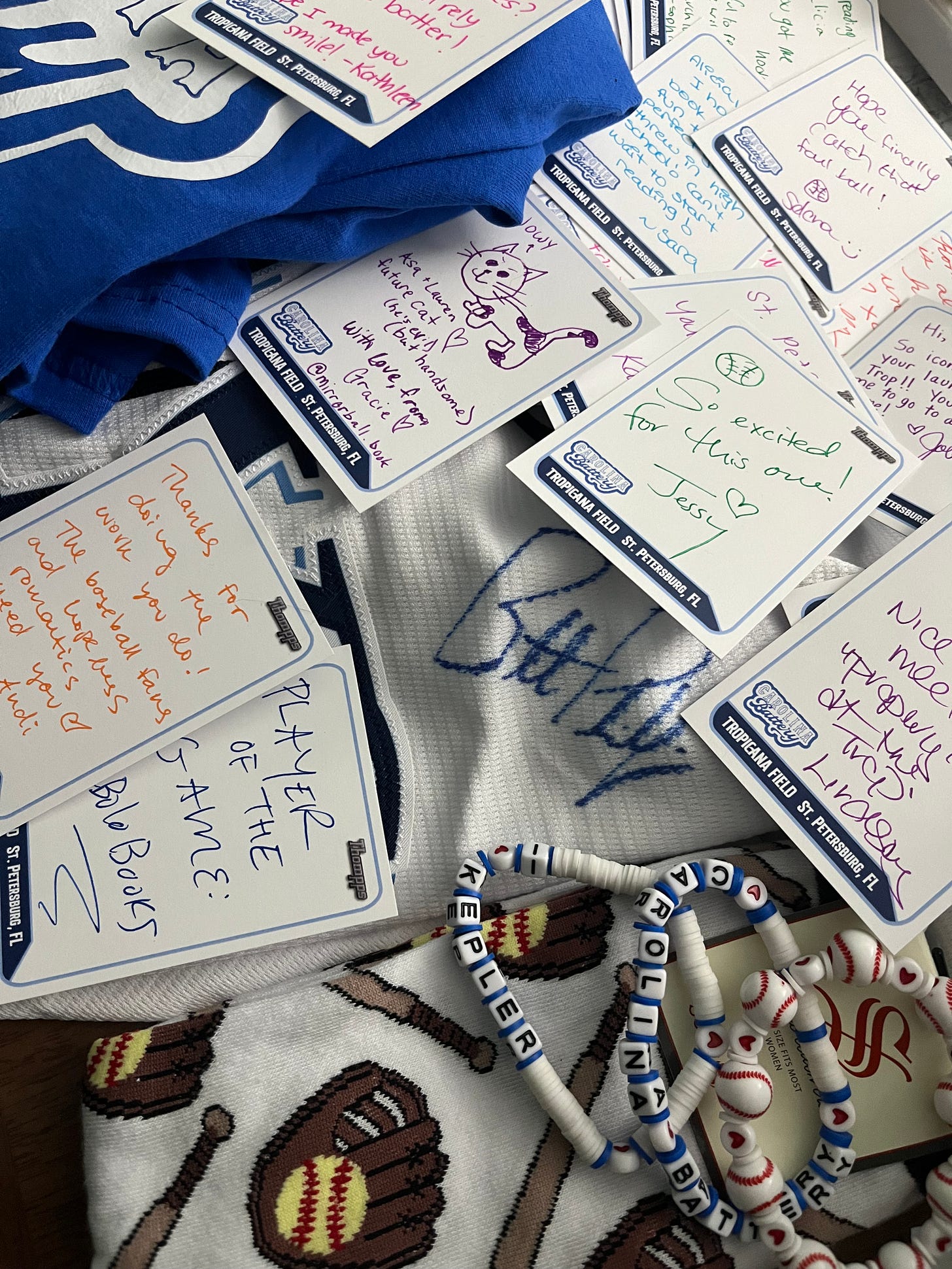 A picture of some of the blank baseball cards people wrote messages on, together with a few other items like a Carolina  Battery t-shirt, a signed Brett Phillips jersey, some friendship bracelets, etc.