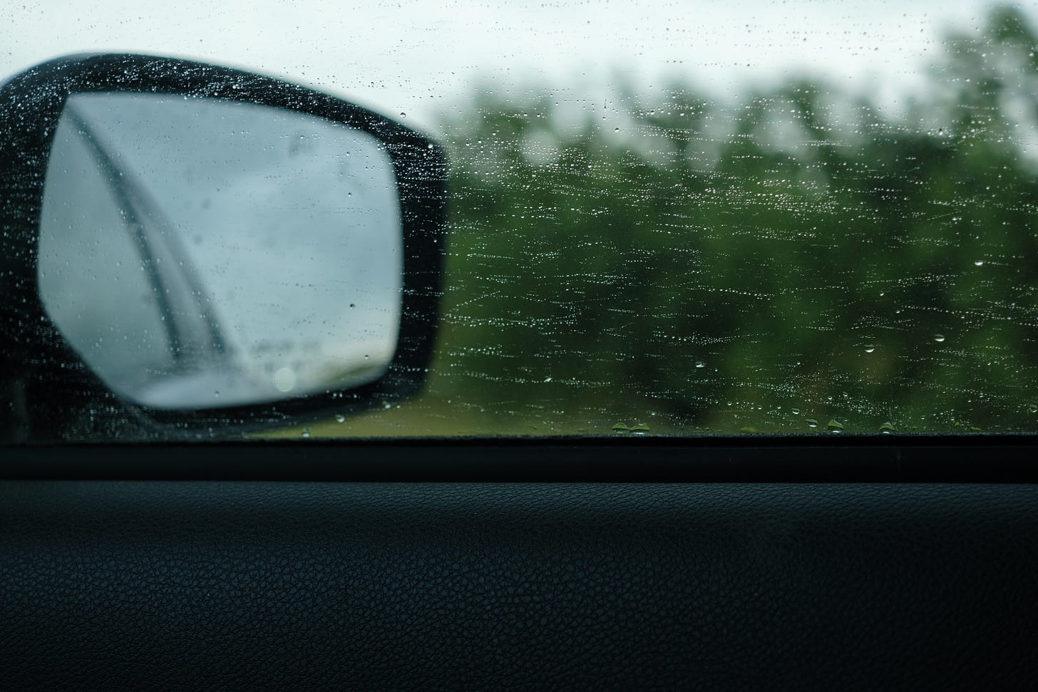 A side view miirror in a moving car with raindrops on the window. 
